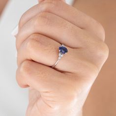 a woman's hand wearing a ring with an oval shaped blue sapphire and diamond accents