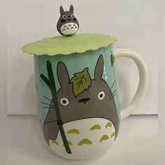 a totoro mug with a green lid and an animal figurine on top