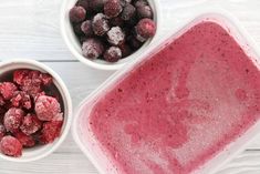 two bowls filled with berries next to each other on top of a white wooden table