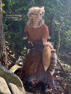 a woman wearing a cat mask and sitting on top of a rock in the woods