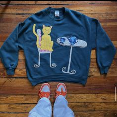 a pair of shoes and a sweatshirt with a cat on it sitting next to a skateboard