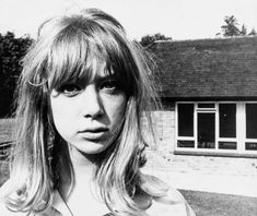 a black and white photo of a woman in front of a house with long hair