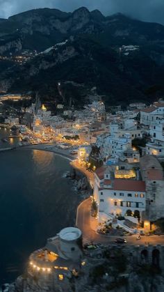 an aerial view of a town by the water at night with mountains in the background