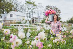 a woman holding a bucket full of flowers in her hands while standing in the middle of a field