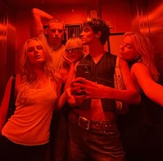 a group of young people standing around each other in a red light room holding wine glasses