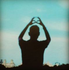 a man holding his hands up in the shape of a heart with buildings in the background