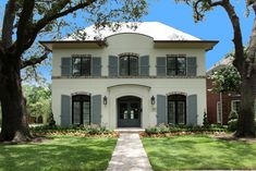 a large white house with blue shutters on the front and side windows, surrounded by green grass