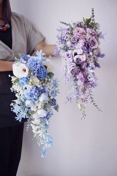 two bouquets of flowers are being held by a woman's hands in front of a white wall