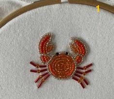 a close up of a crab made out of bead and thread on a piece of fabric