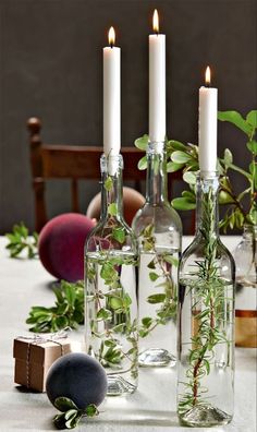 three bottles with plants in them sitting on a table next to rocks and candlesticks