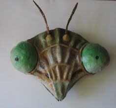 a close up of a green insect on a white wall with two eggs in it's shell