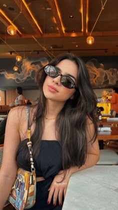 a woman sitting at a table with her hand on her hip wearing sunglasses and holding a purse