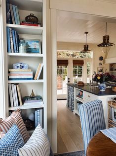 an open kitchen and living room area with bookshelves on the wall, blue striped chairs