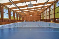 an indoor basketball court with blue tarps and green cones on the floor, surrounded by large windows