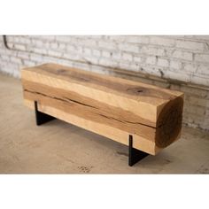 a wooden bench sitting on top of a floor next to a white brick wall with black metal legs