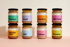 six jars of different kinds of food on a pink countertop, with the labels labeled as almonds, pistachio, and hazelnut