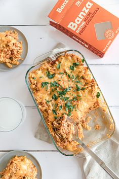 a casserole dish with meat and cheese in it next to two plates on the table