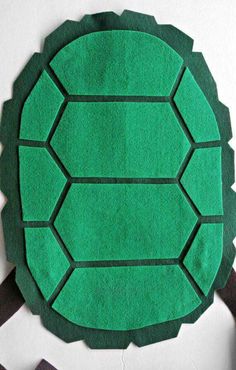 a green turtle made out of felt sitting on top of a white table next to scissors