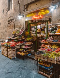 an outdoor market with fruits and vegetables on display in boxes, along side a brick building