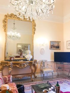 a living room filled with furniture and a chandelier hanging from the ceiling over a flat screen tv