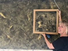 a woman is holding up a painting in front of a wall that has gold paint on it