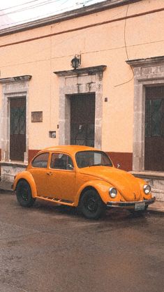 an orange car is parked in front of a yellow building with two doors and windows