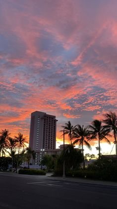 the sky is pink and purple as the sun sets in front of some buildings with palm trees