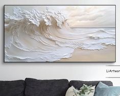 a living room scene with focus on the couch and large painting above it that has an ocean wave