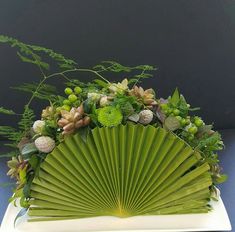 a large green fan sitting on top of a table next to flowers and greenery