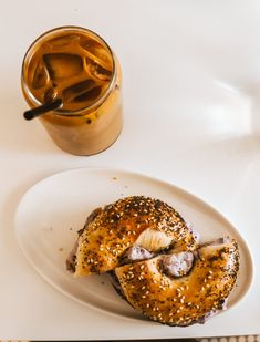 a white plate topped with a bagel covered in sesame seeds next to a cup of coffee