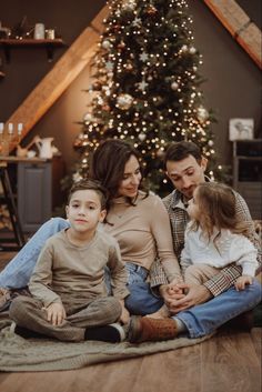 a family sitting on the floor in front of a christmas tree