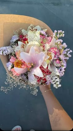 a bouquet of flowers is being held by someone's hand in front of the water