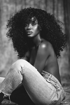 a black and white photo of a woman sitting on the ground with her hair blowing in the wind