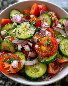 a white bowl filled with cucumbers, tomatoes and onions