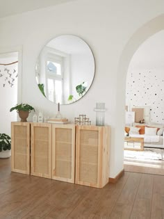 a living room with white walls and wooden furniture in front of a large round mirror