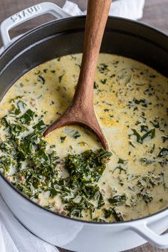 a wooden spoon in a pot filled with cheese and spinach soup on top of a white napkin