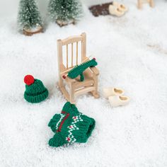 a small wooden rocking chair sitting on top of snow covered ground next to miniature christmas trees