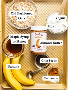 ingredients to make oatmeal are displayed on a baking tray with banana, yogurt, maple syrup, almond butter and cinnamon