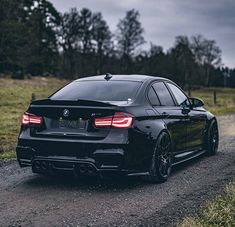 a black bmw parked on the side of a dirt road in front of trees and grass