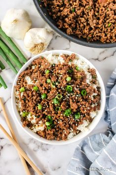 a bowl filled with ground beef and rice next to chopsticks on a marble surface