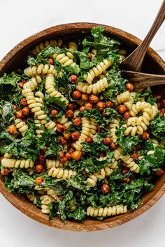 a wooden bowl filled with pasta and greens