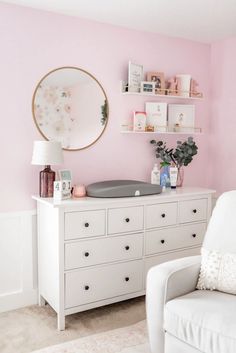 a room with pink walls, white furniture and a round mirror on the wall above it