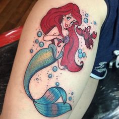 the little mermaid is sitting on top of her leg with an orange fish in it's mouth