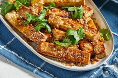 tofu with sesame seeds and greens on a white plate next to a blue napkin