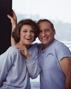 an older man and woman are posing for a photo in front of a window with their arms around each other