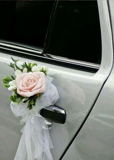 a pink rose tied to the side of a white car with ribbon and flowers on it