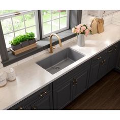 a kitchen sink sitting under a window next to a counter top with flowers on it