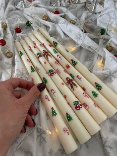 a hand is holding seven white candles with christmas decorations on them, and the candle sticks are lined up next to each other