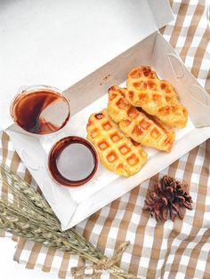 some waffles and syrup are sitting on a checkered tablecloth with pine cones