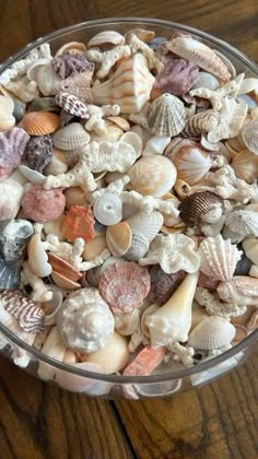 a glass bowl filled with lots of different colored seashells on top of a wooden table